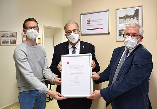 Prof. Wolfgang Schareck (Mitte, Universität Rostock) erhält von Prof. Steffen Emmert (re.) und Dr. Lars Böckmann (links, Universitätsmedizin Rostock) die Ehrenmitgliedsurkunde des NZPM.